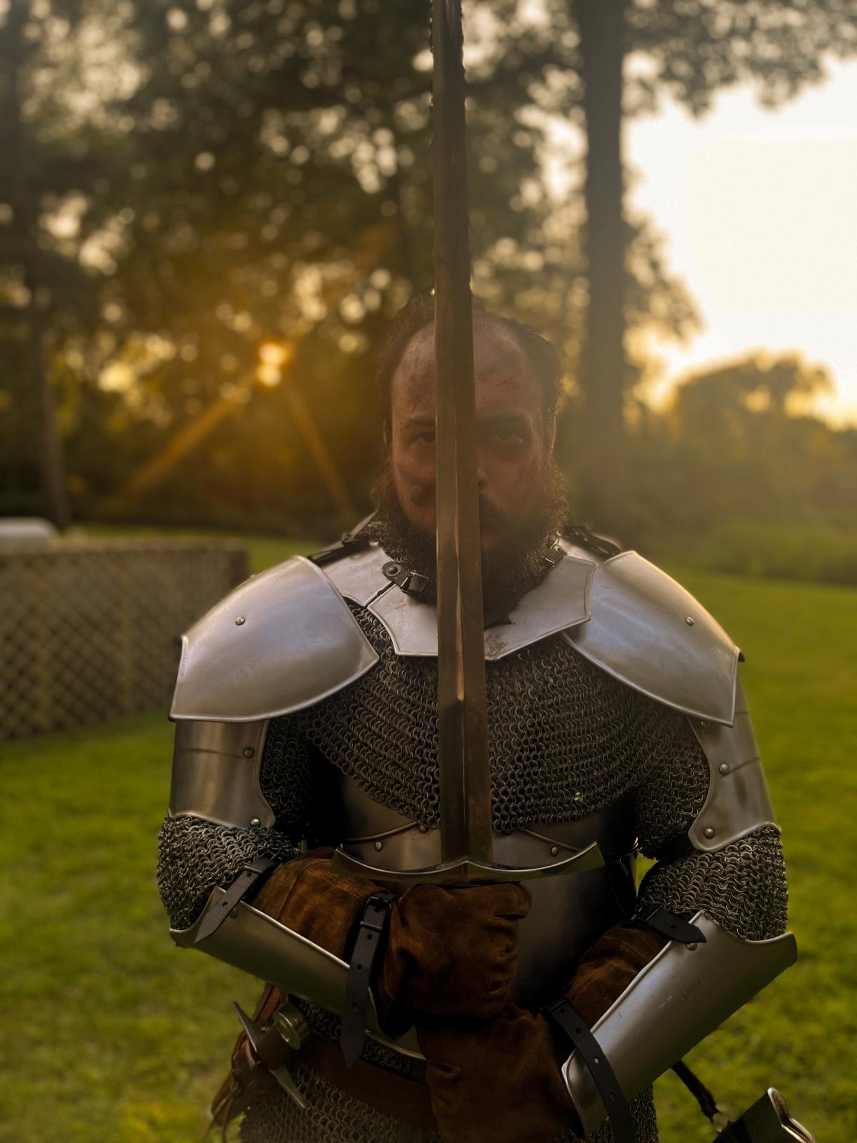 A knight in shining armor holding his sword in front of him bathed in a glorious sunset